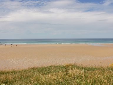 A sandy beach with a few people and the sea in the background with grass in the foreground at Little May in Newquay
