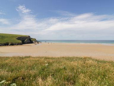A sandy beach with grassy cliffs in the foreground and ocean in the background at Little May in Newquay