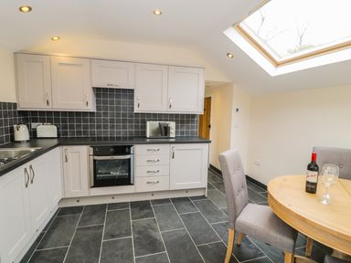 A kitchen with white cabinets a black tiled backsplash a built in oven a microwave toaster kettle dining table with chairs and skylight at Bothi in Llanuwchllyn
