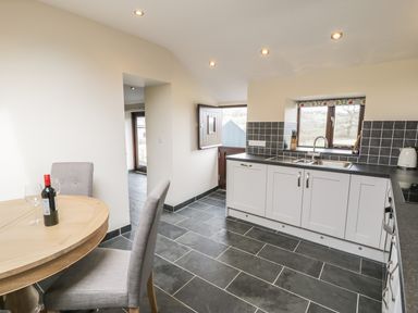 A kitchen with a wooden dining table and chairs and a countertop with a sink and window at Bothi in Llanuwchllyn