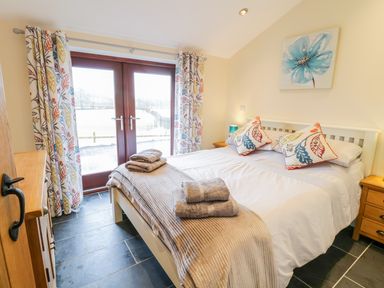 A bedroom with a double bed with towels on it wooden nightstands and patterned curtains at Bothi Llanuwchllyn