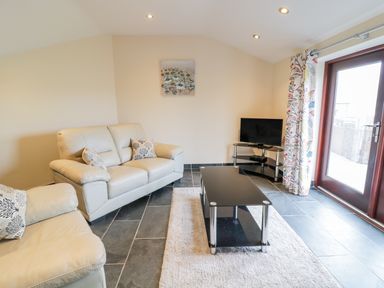 A living room with cream sofas a black glass coffee table a TV on stand and a glass door with floral curtains at Bothi in Llanuwchllyn