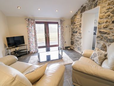 A living room with leather sofas glass coffee table and television near stone wall at Bothi in Llanuwchllyn