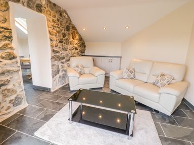 A living room with a leather sofa and armchair a black glass coffee table and a stone wall at Bothi in Llanuwchllyn