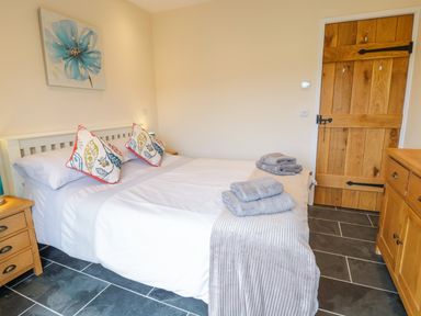 A bedroom with a bed featuring decorative pillows and folded towels a wooden door and furniture a painting of a blue flower above the bed at Bothi in Llanuwchllyn