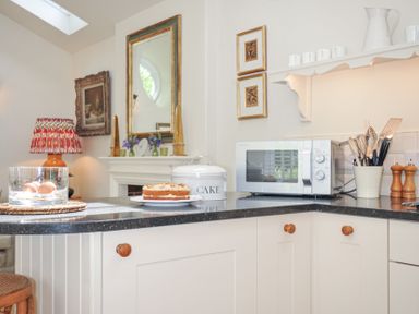 A kitchen with a microwave and cake on the counter at The Coach House at Pendower House Fowey
