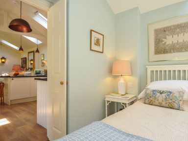 A bedroom with a bed and side table leading to a kitchen at The Coach House at Pendower House Fowey