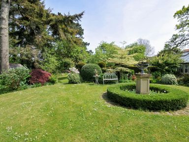 A garden with trees, bushes, and a sundial at The Coach House at Pendower House Fowey