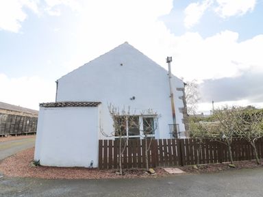 White building with a small brown fence and leafless trees in front at Chillingham Cottage in Belford