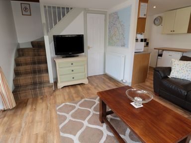 A living room with a plaid carpeted staircase a small television on a chest of drawers a wooden coffee table and a black leather sofa at Chillingham Cottage in Belford
