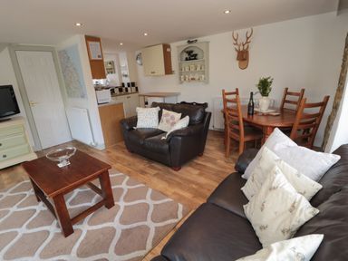 A living room with two dark leather sofas a wooden coffee table a dining table with chairs and a small kitchen area at Chillingham Cottage in Belford