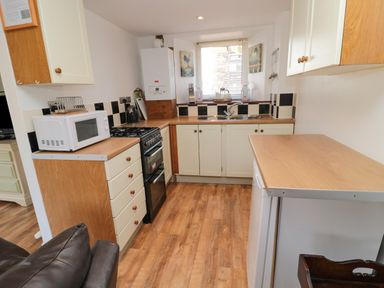 A kitchen with wooden countertops white cabinets a microwave stove sink and window at Chillingham Cottage in Belford