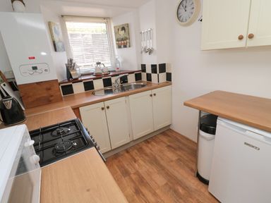 A small kitchen with a gas stove microwave sink countertop and refrigerator at Chillingham Cottage in Belford
