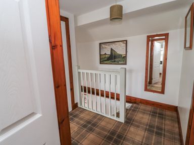 A hallway with a white railing a framed photo on the wall a mirror and plaid carpet at Chillingham Cottage in Belford
