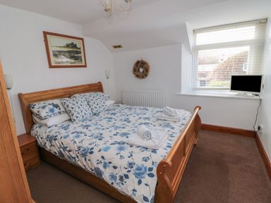 A bedroom with a wooden bed with floral bedding a window with blinds a small television on the windowsill and framed artwork on the wall at Chillingham Cottage in Belford