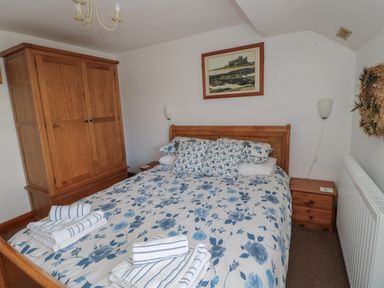 A bedroom with a wooden bed with floral bedding two bedside tables a wooden wardrobe and a framed picture at Chillingham Cottage in Belford