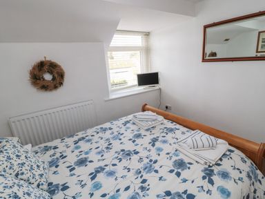 A bedroom with a wooden bed covered with floral bedding towels on the bed a small tv on the windowsill a wall mirror and a wreath on the wall at Chillingham Cottage in Belford