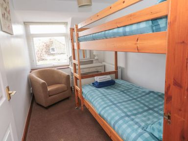 A small bedroom with wooden bunk beds a beige armchair and a white dressing table at Chillingham Cottage in Belford