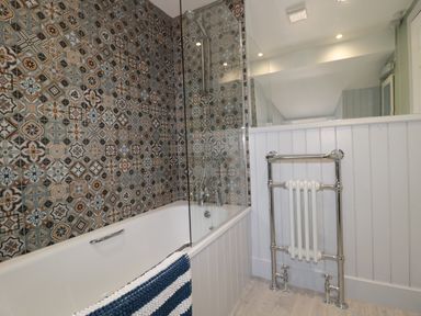 A bathroom with a bathtub featuring patterned tiles and a towel rail at Chillingham Cottage in Belford