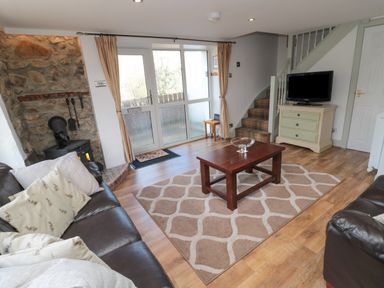 A living room with brown leather sofas a wooden coffee table a rug a wall-mounted stove a television on a dresser and stairs at Chillingham Cottage in Belford