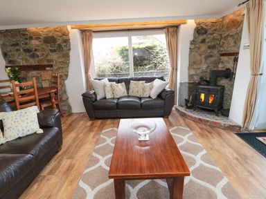 A living room with leather sofas a wooden coffee table stone walls and a wood burning stove at Chillingham Cottage in Belford