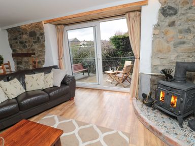 A living room with a leather sofa and wood burning stove next to patio doors opening to outdoor seating at Chillingham Cottage in Belford