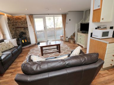 A living room with leather sofas a wooden coffee table a wood stove and a TV next to stairs at Chillingham Cottage in Belford