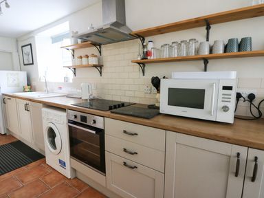 A kitchen with a microwave oven washing machine electric stove sink and shelves with jars and glasses at Pengraig near Tregaron