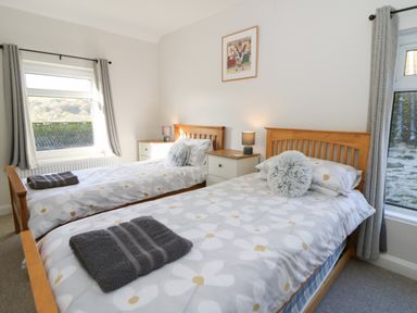 A bedroom with two single beds bedside tables lamps and windows with grey curtains at Pengraig near Tregaron