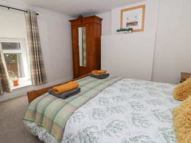 A bedroom with a bed, folded towels, a wooden wardrobe, a window with curtains, and a framed picture at Pengraig near Tregaron