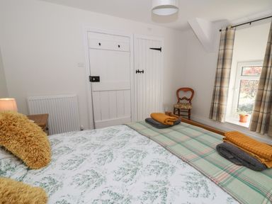 A bedroom with a bed with pillows and folded towels a wooden chair by a window with plaid curtains at Pengraig near Tregaron