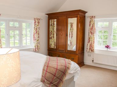 A bedroom with a large wooden wardrobe with mirrors two windows with floral curtains a bed with a blanket and a lamp at The Old Farmhouse Upper Pitts Knighton