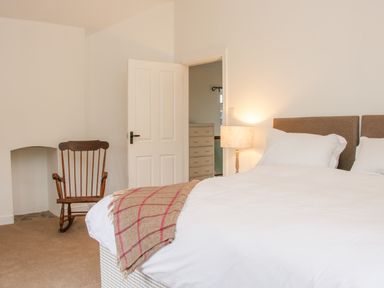 A bedroom with a bed lamp rocking chair and an open door revealing a chest of drawers at The Old Farmhouse Upper Pitts in Knighton