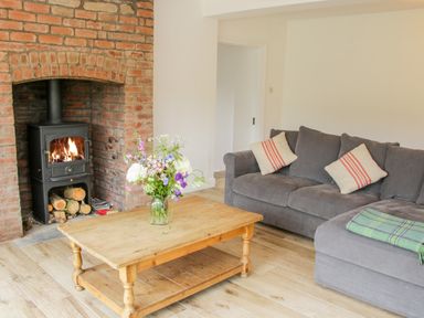 A living room with a wooden coffee table with flowers a gray sofa with cushions and a wood burning stove in a brick fireplace at The Old Farmhouse Upper Pitts in Knighton