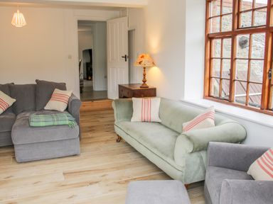 A sitting room with a green sofa gray chairs wooden flooring and a wooden side table with a lamp at The Old Farmhouse Upper Pitts in Knighton