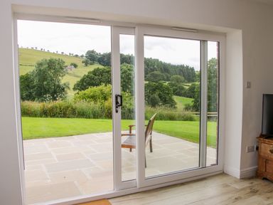 A patio with a wooden chair outside sliding glass doors overlooking a garden and countryside at The Old Farmhouse Upper Pitts in Knighton