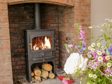 A wood-burning stove with fire inside set in a brick fireplace next to a bouquet of flowers at The Old Farmhouse Upper Pitts Knighton