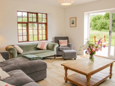 A living room with sofas armchair ottoman wooden coffee table with flowers and large windows at The Old Farmhouse Upper Pitts in Knighton