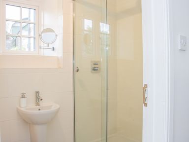 A bathroom with a pedestal sink soap dispenser window round mirror and a glass enclosed shower at The Old Farmhouse Upper Pitts Knighton