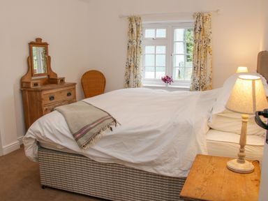 A bedroom with a bed bedside table lamp wooden dresser mirror chair and window with curtains at The Old Farmhouse Upper Pitts in Knighton
