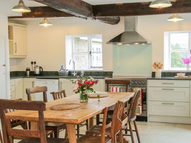 A kitchen with wooden chairs around a table and flowers in a jar on the table at The Old Farmhouse Upper Pitts in Knighton