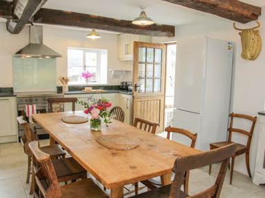 A kitchen with a wooden dining table and chairs a refrigerator and stove with a window and wooden door at The Old Farmhouse Upper Pitts Knighton