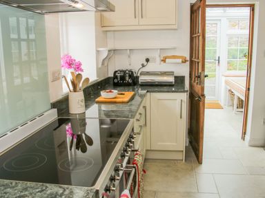 A kitchen with a stove a bowl on a cutting board and wooden spoons in a container at The Old Farmhouse Upper Pitts in Knighton