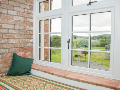 A window seat with a cushion and patterned fabric next to a brick wall overlooking a green landscape at The Old Farmhouse Upper Pitts in Knighton