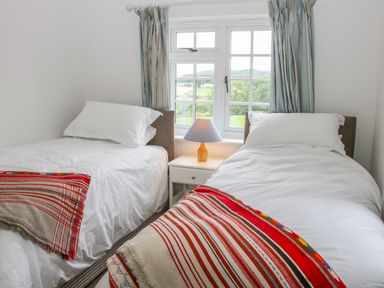 A bedroom with two single beds a nightstand and a lamp under a window at The Old Farmhouse Upper Pitts in Knighton
