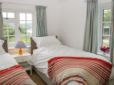 A bedroom with two single beds a bedside table with a lamp and windows with curtains at The Old Farmhouse Upper Pitts Knighton