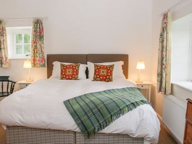 A bedroom with a double bed two bedside tables with lamps floral curtains and a window at The Old Farmhouse Upper Pitts in Knighton