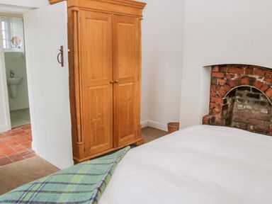 A bedroom with a wooden wardrobe a bed with a green plaid blanket and a brick fireplace at The Old Farmhouse Upper Pitts in Knighton