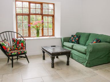 A sitting area with a green sofa and black chair with floral cushions and a wooden coffee table near a window at The Old Farmhouse Upper Pitts in Knighton