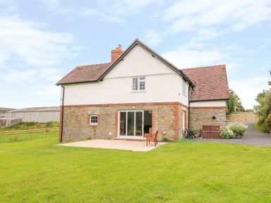 A stone and white two-story house with a tiled roof and a patio with a chair at The Old Farmhouse Upper Pitts in Knighton